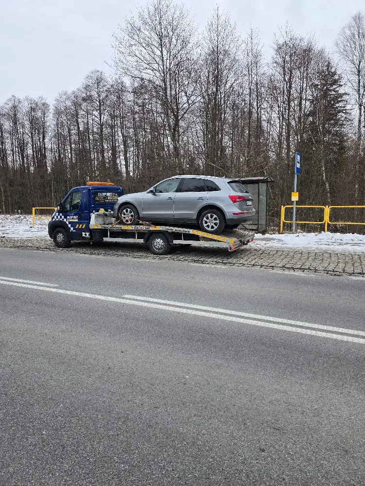 Audi Q5 na platformie lawety przy zaśnieżonej drodze wojewódzkiej zimą.